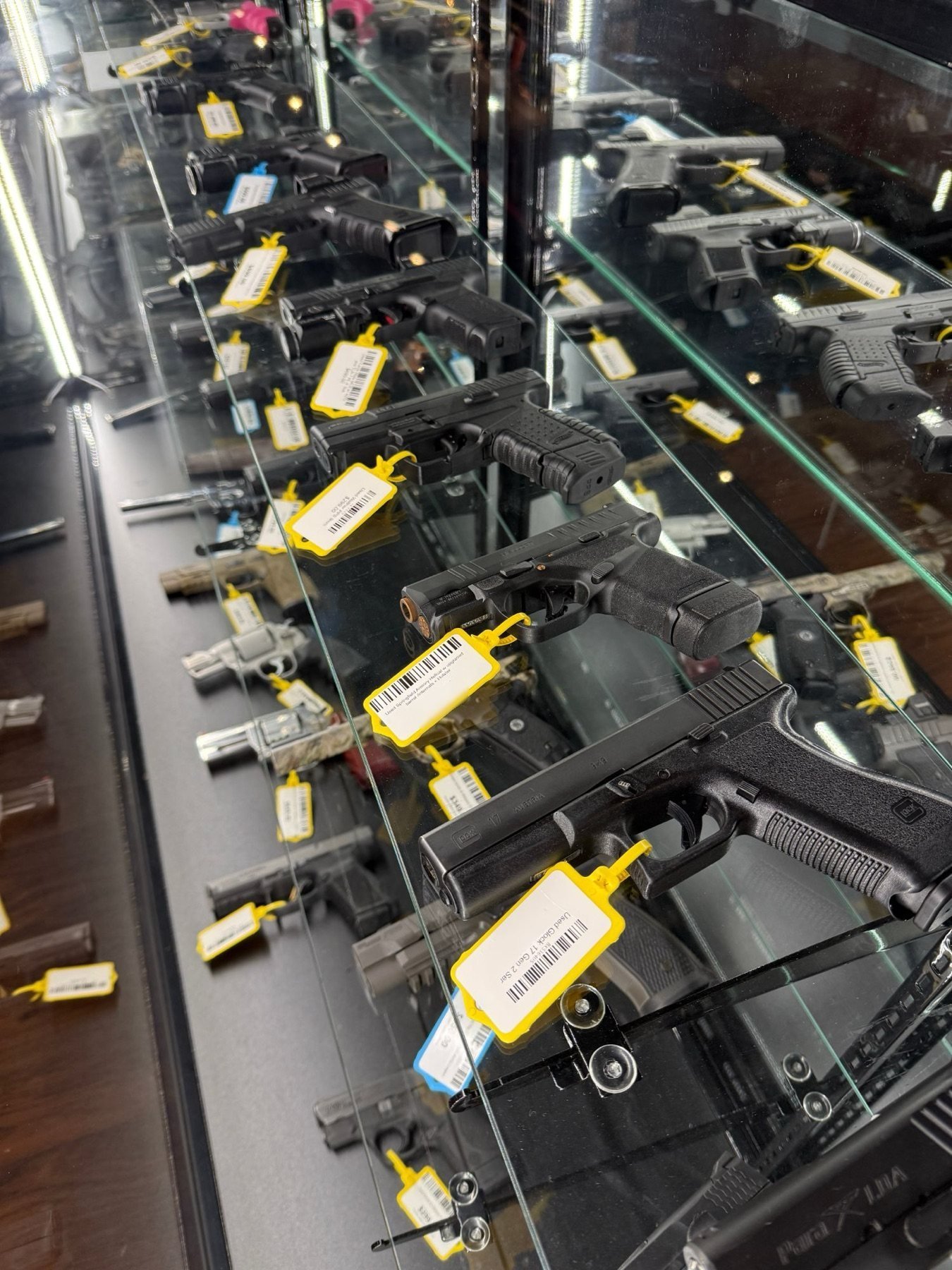 Used handguns with yellow price tags in a lit display case at Liberty Ordnance Supply